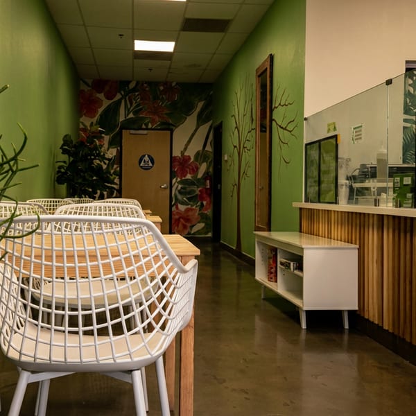 A cafe interior with green walls, white chairs, wooden tables, and a counter with coffee-themed signs.