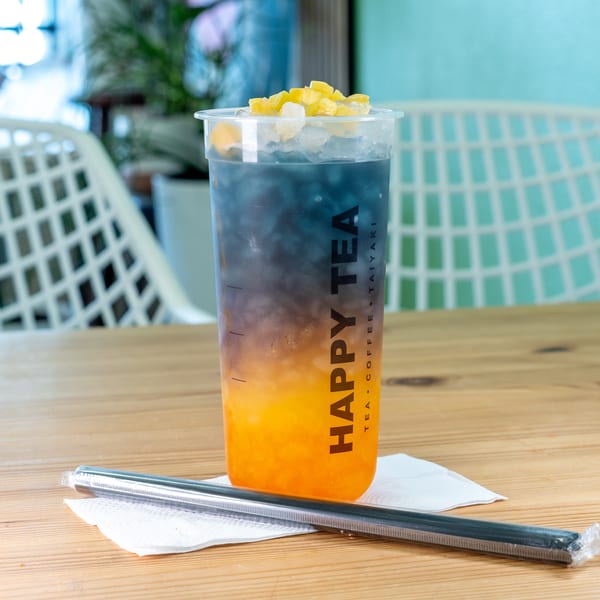 Happy Tea's colorful layered drink with blue and orange liquid, topped with fruit and ice.