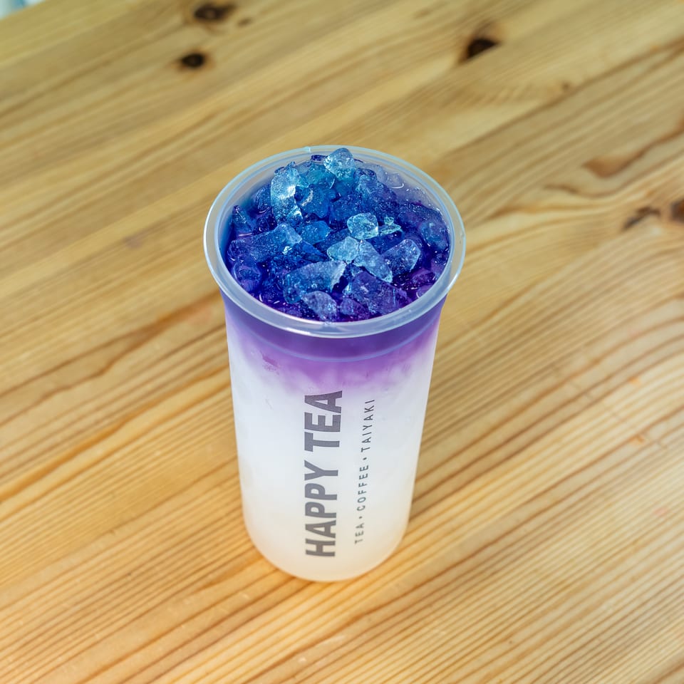 Purple iced drink in a Happy Tea cup sits on a rustic wooden table.