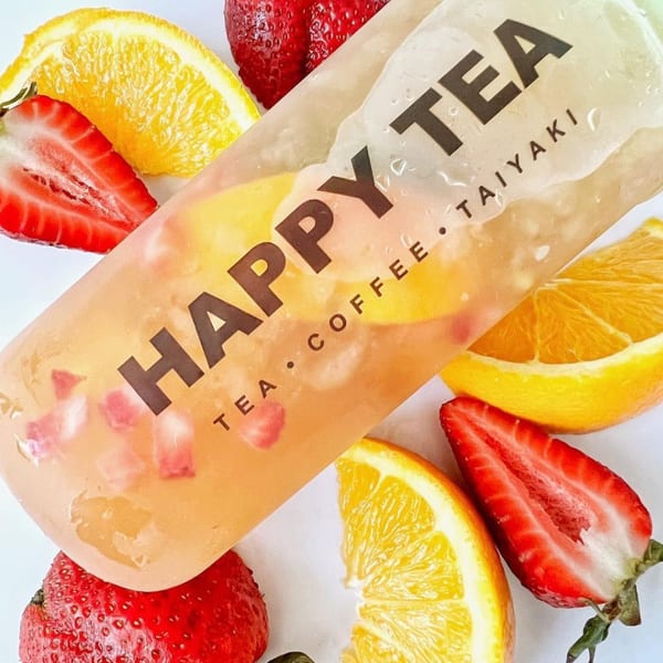 Happy Tea drink with fruit pieces, surrounded by fresh strawberries and orange slices.