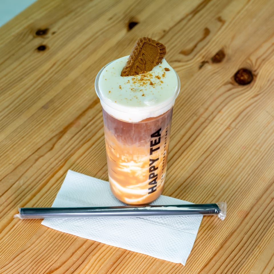 Layered iced drink topped with whipped cream, cinnamon, and a cookie, served on a wooden table with a straw.