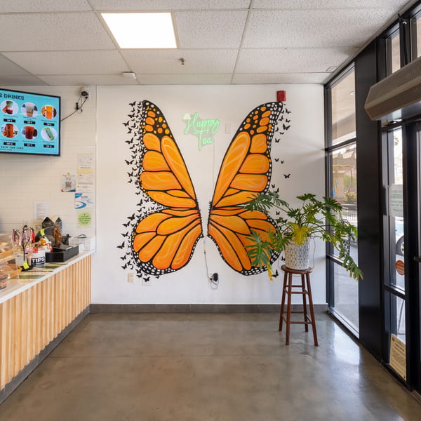 Happy Tea Cafe interior with a butterfly mural, menu screen, counter, and large windows.