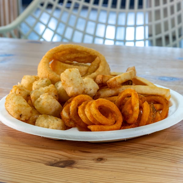 A white plate filled with golden fried onion rings, tater tots, curly fries, and straight-cut fries.