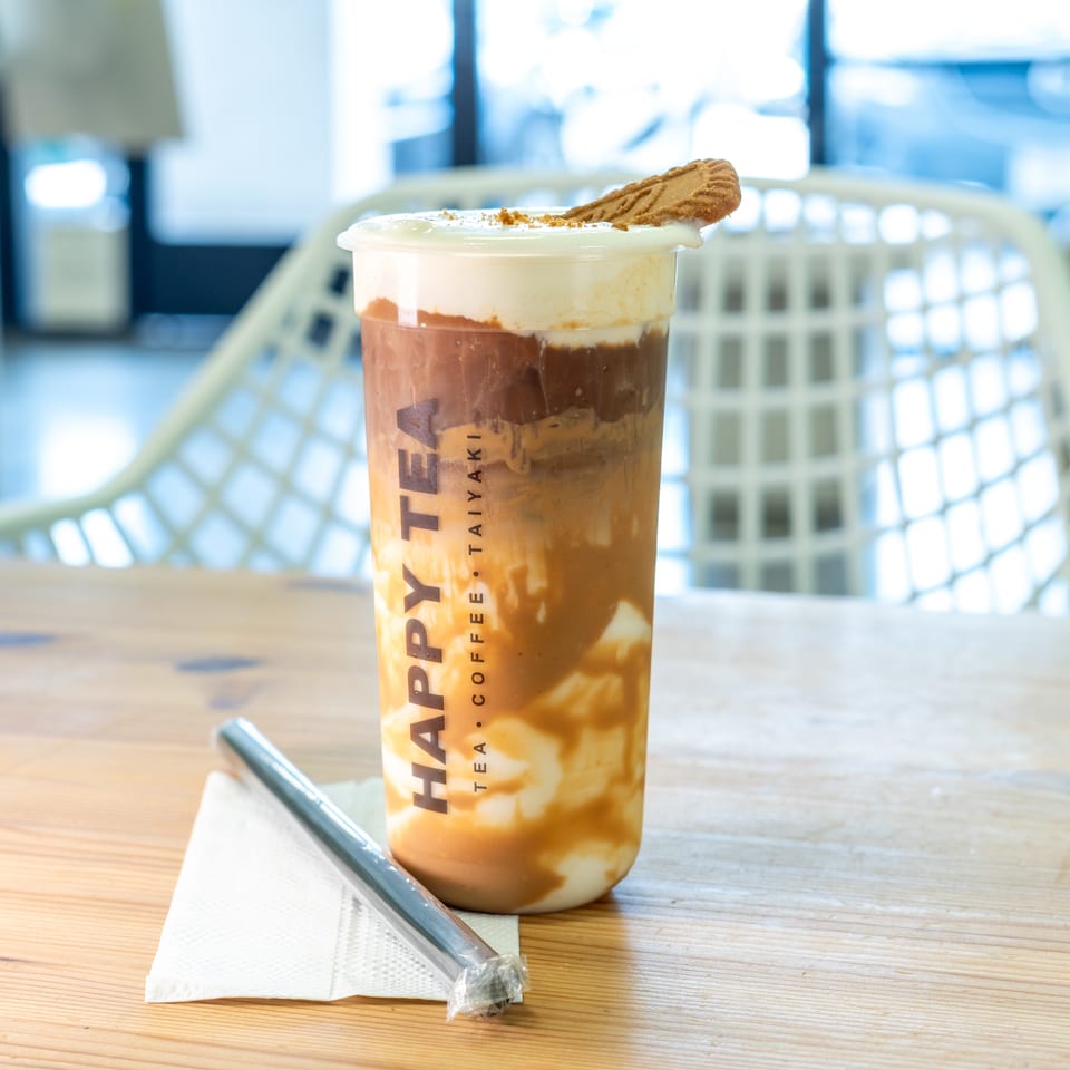 Layered iced coffee drink topped with cream and a cookie, served in a branded cup on a wooden table.