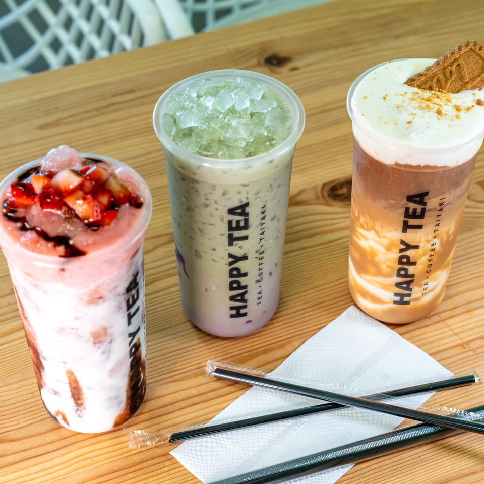 Three colorful Harpy Tea drinks sit on a wooden table, topped with fruit, crushed ice, whipped cream, and a cookie.